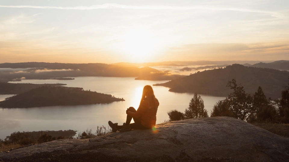 A woman peacefully watching a sunset over a lake, symbolizing the stability achieved through comprehensive mental health services.